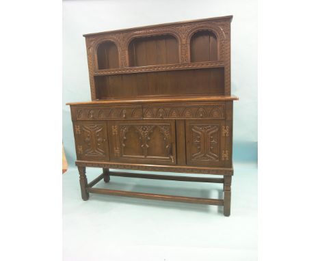 A 1920's Tudor-style dark oak dresser, single over-shelf above cupboard base with two drawers, the whole carved with leafage,