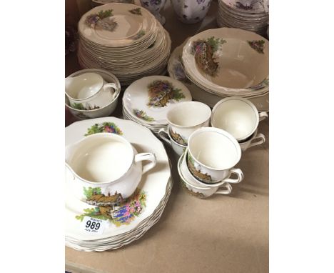 A traditional vintage English ceramic diner and tea set decorated with rural cottages in a floral garden in the style of Ann 