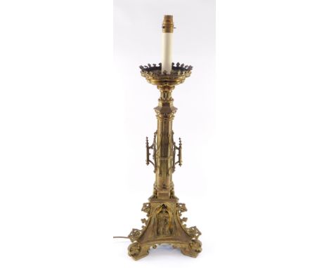 A Victorian Gothic brass alter candlestick, converted to a table lamp, of out swept architectural form, embossed to the base 