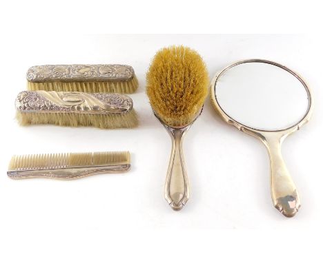 A George V silver backed hand mirror and clothes brush, Birmingham 1921, two silver backed clothes brushes, embossed with flo