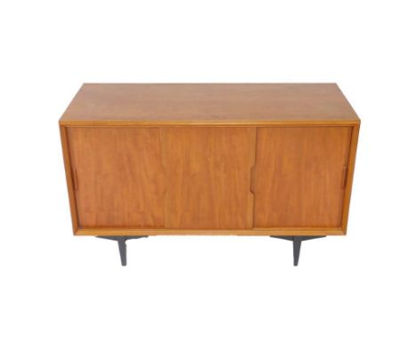 A 1960's teak sideboard, with three sliding doors enclosing a single shelf and short drawer, raised on tapering square black 