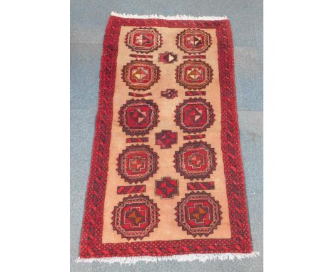 A Balouch rug, with red geometric medallions against a light brown ground, 155cm x 88cm.
