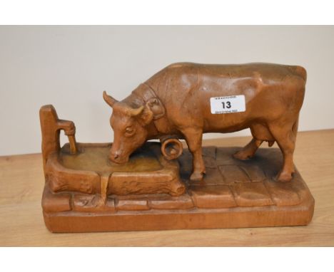 A carved wooden cow, depicted drinking from trough.