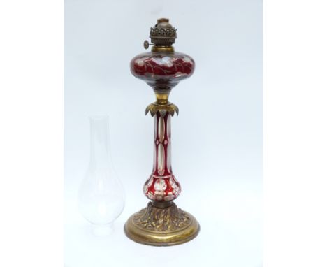 A gilt metal and flash overlaid glass lamp, the base with oak leaf decoration and the shaft and bowl cut with ruby staining o