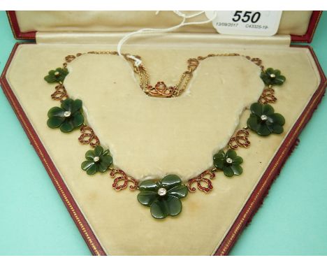 A 9ct gold necklace made up of jade clover leaves set with a diamond to the centre of each and alternating red enamel bow sec