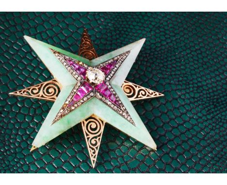 An art deco jadeite jade, ruby and diamond star brooch, with central claw set old cut diamond within a ruby pave setting and 