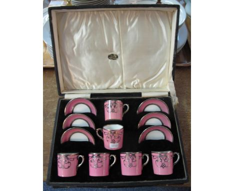 Set of six Aynsley miniature coffee cans and saucers on a pink ground with white metal mounts and decoration. In fitted case.