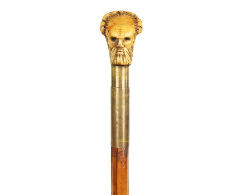 A 19TH CENTURY SWORD STICK with a mask head carved antler handle, brass collar and cane shaft revealing a steel triform blade