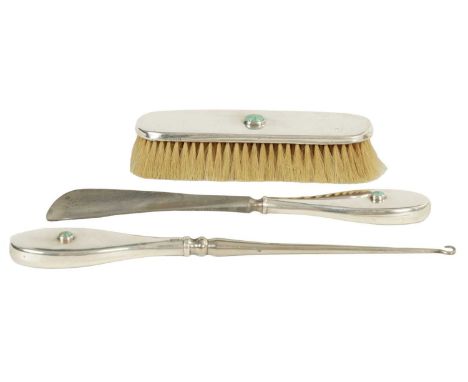 AN ART NOUVEAU SILVER DRESSING TABLE SET WITH RUSKIN JEWELS comprising a brush, shoe horn and button hook-each set with a cab