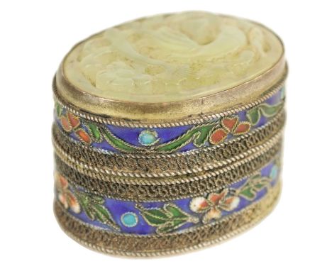 A CHINESE SILVER ENAMEL PILL BOX WITH CARVED JADE TOP depiciting a bird amongst trees, the sides decorated with coloured flor
