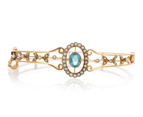 EDWARDIAN BANGLE, EARLY 20TH CENTURY set with an oval zircon in a surround of seed pearls and flanked with pearl set floral d