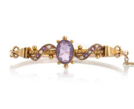 EDWARDIAN AMETHYST AND SEED PEARL BANGLE, IN NINE CARAT GOLD the hinged bangle set with a central oval shaped cushion cut ame