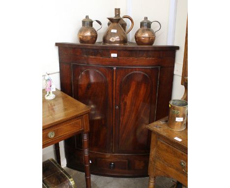 A 19th Century mahogany bow fronted corner cupboard, the interior shelves enclosed by a pair of arched panelled doors, single