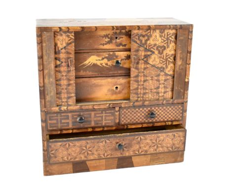 A Japanese parquetry inlaid trinket cabinet with tambour front enclosing three drawers with scene of mount Fuji, above two sh