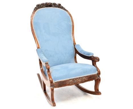A Victorian walnut open arm rocking chair upholstered in a light blue velour with carved floral motifs and scroll ends.