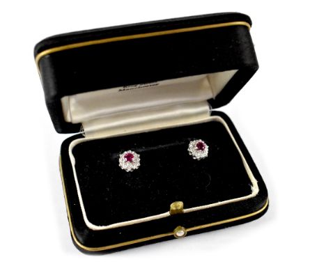 A pair of white metal floral ear studs set with central ruby-coloured stone and white stones.