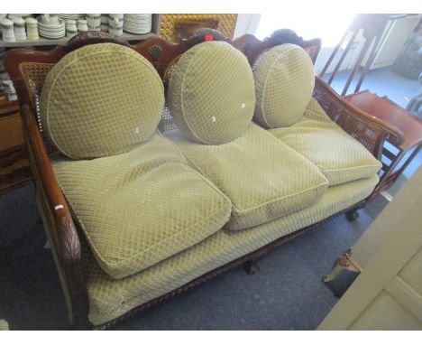 An early 20th century Bergere suite consisting of a sofa and two matching armchairs, having scroll shaped arms and standing o