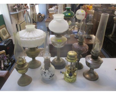 A group of seven vintage oil lamps to include a brass column lamp with a floral painted milk glass reservoir, on a black colo