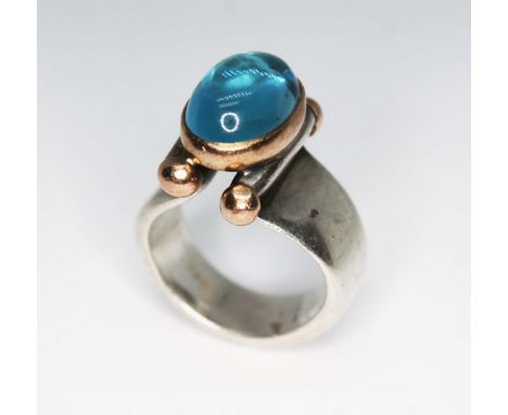 A Modernist silver ring set with a blue topaz cabochon, sponsor's mark 'GL', London 2004, gross wt. 18.34g, size O/P.  Condit