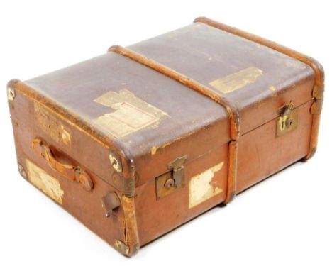 An early 20thC pressed leather travel trunk, with wooden and metal mounts, with side carrying handles and part luggage label,