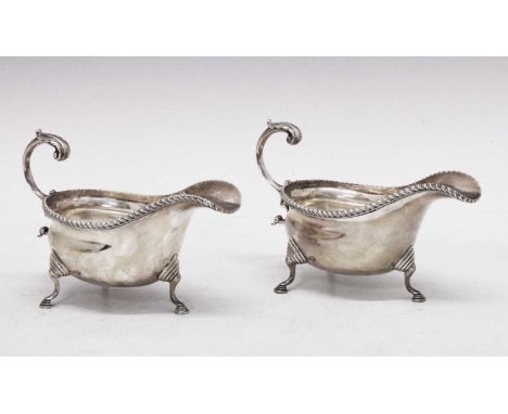Pair George V silver sauceboats with gadrooned rim, leaf-capped open scroll handle and standing on three shaped legs with ree