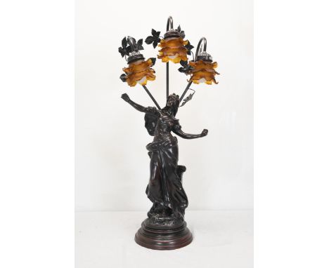 A 20th century spelter classical figural three branch table lamp, the floral shades of moulded amber glass. H.86 W.34 D.20cm.