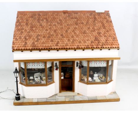 A doll's bakery featuring two clothed figures, shop counter, shelves and two chairs, accessories including scales and telepho