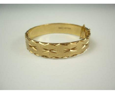 A 9ct gold hinged bangle, the textured face being decorated with a repeating bright-cut star design, within a conforming bord