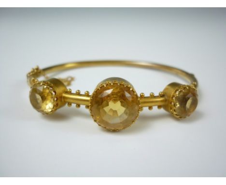 A Victorian yellow metal and citrine hinged bangle, centrally faced with a crown set stone of approximately 5ct, flanked by t