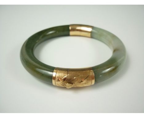 A 14K gold and polished jade hinged bangle, the mounts bearing engraved foliate decoration, with the spring lock opening on a