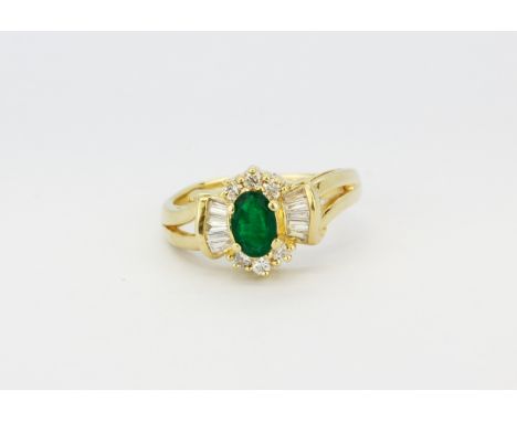 A 14ct yellow gold (stamped 14k) ring set with an oval cut emerald surrounded by round and baguette cut diamonds, (L.5).