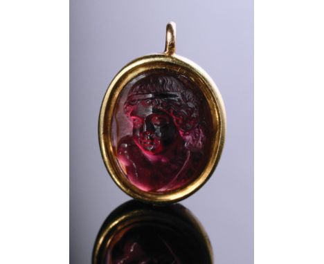 A carved ruby pendant, the oval ruby with a relief carved bust figure of a cherub, in reeded yellow metal mount