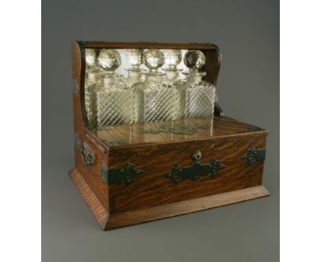A late Victorian oak and brass bound tantalus/humidor, having a bevelled mirror plate reflecting three moulded bottles behind
