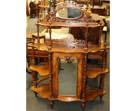 A Victorian figured walnut serpentine chiffonier whatnot, having a fret carved mirror and shelf superstructure above mirrored