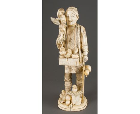 A late 19th century Japanese ivory okimono, carved as a toy seller, holding a puppet, with tray slung from his shoulders supp