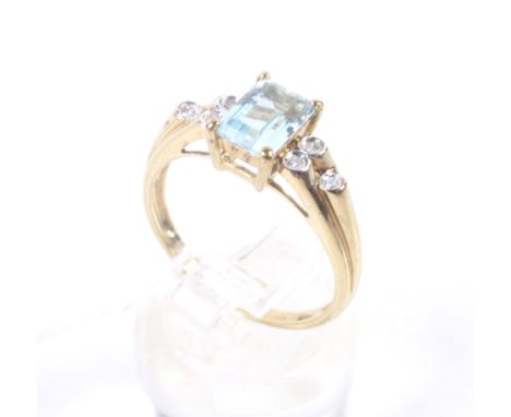 A 9ct gold, topaz and diamond dress ring. Centred with a rectangular step-cut pale blue topaz between small round brilliant d