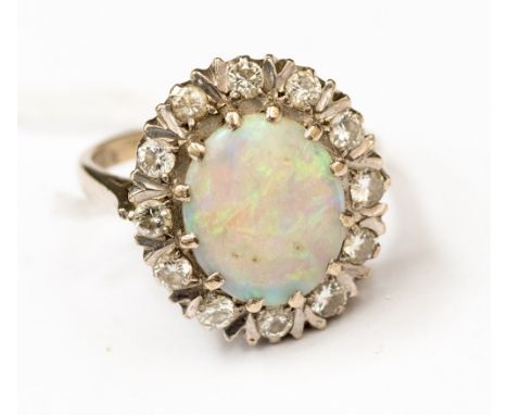 An opal and diamond cluster ring with a central opal size approx 9x11mm with green and blue tone, surrounded by diamonds and 