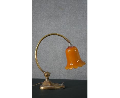 An Edwardian brass desk lamp, with an orange glass shade, on a curved stem, with a heart shaped base. H.38 W.36cm 