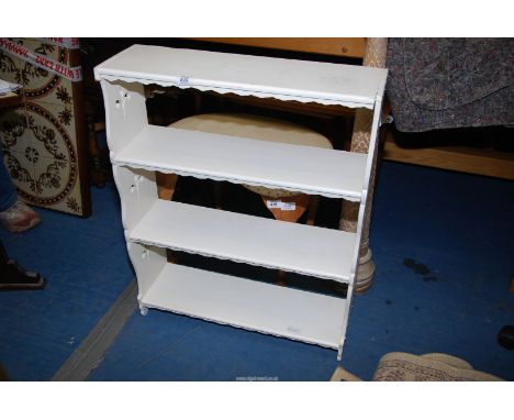 A white painted wall shelf unit having four scalloped edge shelves.