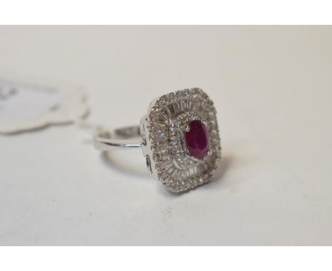 An 18ct white gold, ruby and diamond cluster ring, the oval ring within surrounds of brilliant and baguette cut diamonds, app