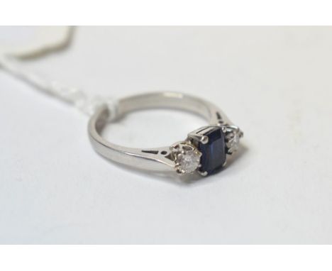 A sapphire and diamond ring, the centre baguette cut stone flanked by two modern brilliant cut stones, in a white coloured me