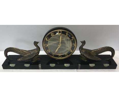 A French Art Deco mantle clock on a black marble onyx base with gilt metal confronting peacocks. 60 l x 22 h x 9cms d. 