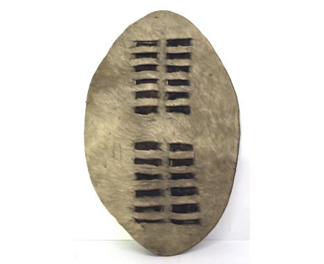 A Zulu igqoka shield, of stiffened cowhide, with traditional slots cut into front, into which is inserted a darker coloured h