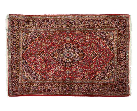 A red ground Kashan rug with central mandorla and corners on a field of Arabesques within a broad palette border and fringed 