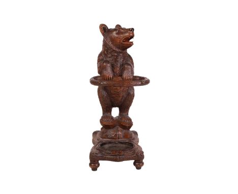 A carved wood Black Forest stick stand, modelled as a bear, its head set with glass eyes and an open mouth, holding a branch-