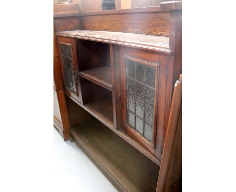 An Arts &amp; Crafts oak bookcase with two leaded glazed doors flanking single shelf and raised on spade feet, width 107cm.