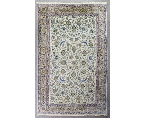 A Kashan carpet woven in pastel shades with palmettes and trailing leaf and floral design on an ivory ground within conformin