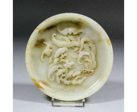 A Chinese celadon jade circular shallow dish with some brown inclusions, the interior finely carved in bold relief with three