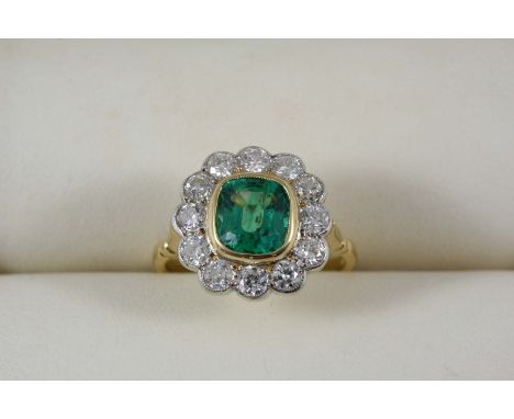 AN EMERALD AND DIAMOND CLUSTER RING the rounded square-shaped emerald is set within a surround of twelve circular-cut diamond