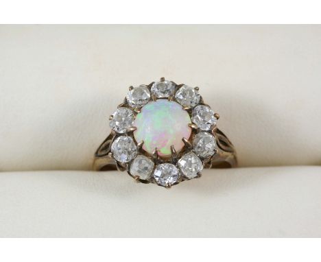 AN OPAL AND DIAMOND CLUSTER RING the circular white cabochon opal is set within a surround of ten cushion-shaped diamonds, in